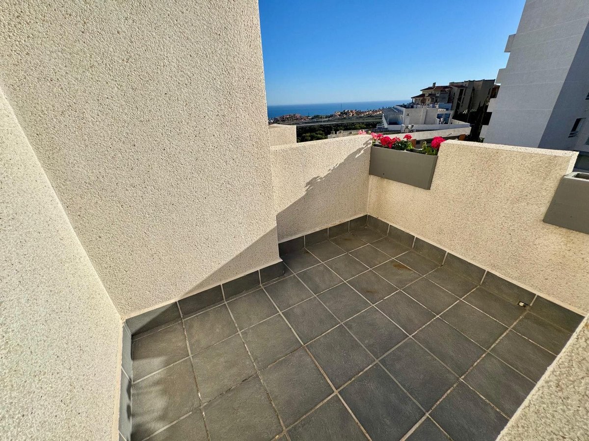 A tiled balcony with flower planters, overlooking the sea and buildings under a clear blue sky.
