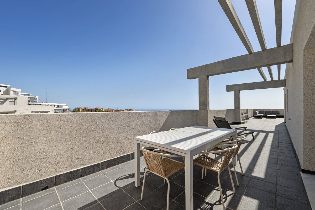 Outdoor terrace with dining table and chairs, lounge seating, and a view of the sea under a clear blue sky.