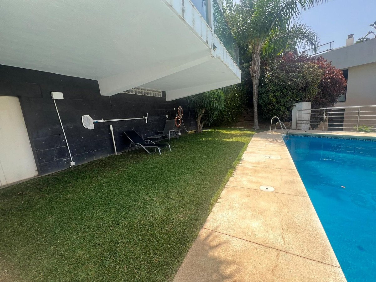 Outdoor area with a swimming pool, a green lawn, lounge chairs, and surrounding vegetation.