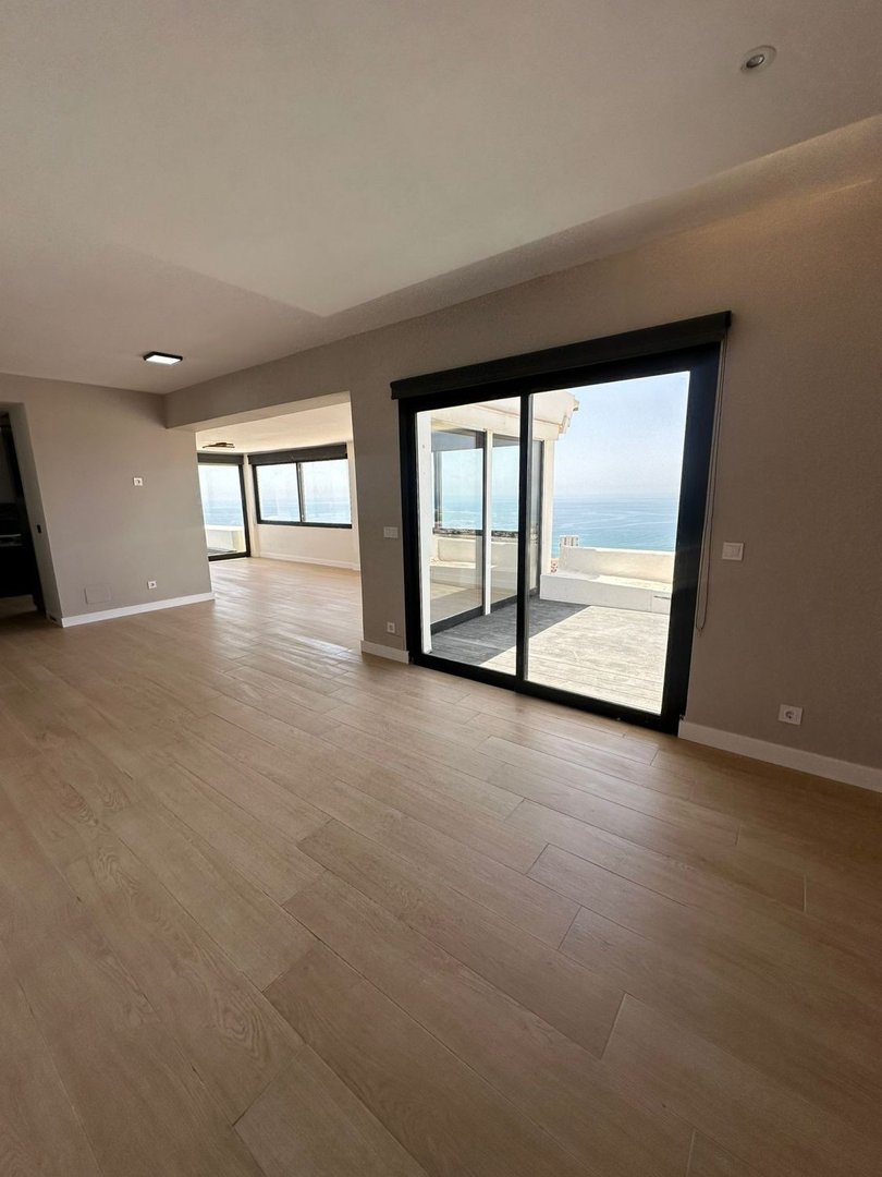 Spacious living room with modern flooring and large sliding doors opening to a terrace with a stunning sea view.