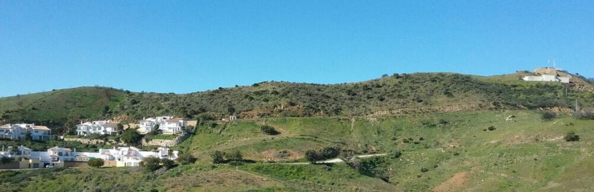 A panoramic view of white houses nestled on green hills under a clear blue sky.