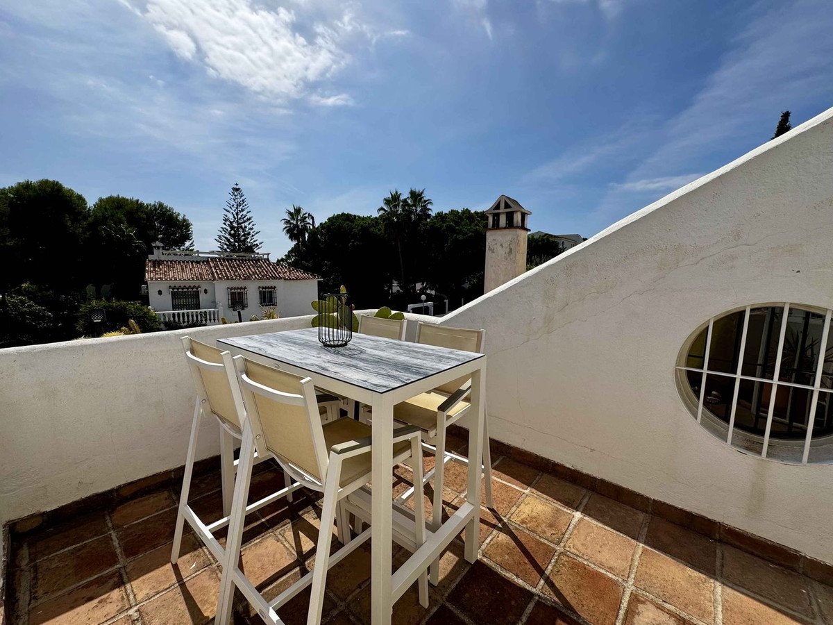 A modern outdoor dining set on a tiled terrace overlooks trees and a Mediterranean-style house.