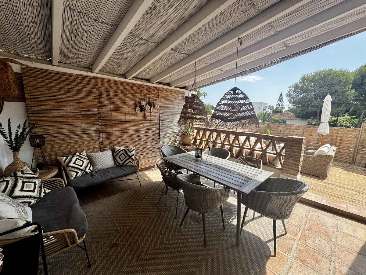 A covered terrace with dining table and chairs, sofa, and outdoor seating, featuring natural bamboo walls and woven pendant lights.