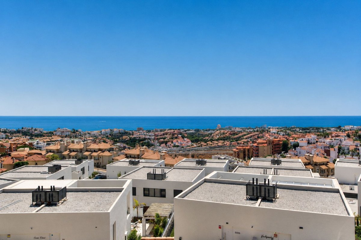 Modern white homes with flat roofs, overlooking a coastal town and the blue sea under a clear sky.