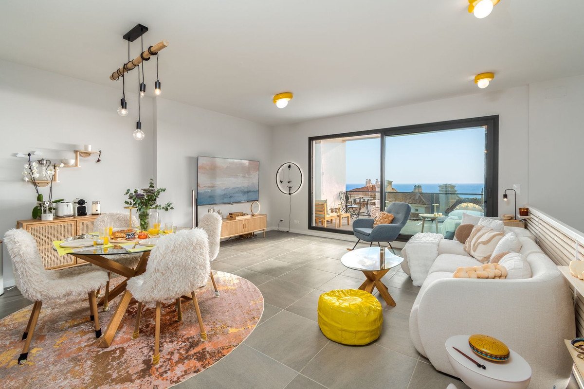 Modern living and dining area with plush seating, a glass table, and a balcony with a sea view.