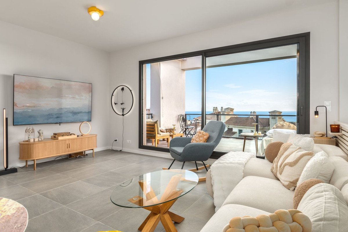Modern living room with comfortable sofa, armchair, and large sliding doors opening to a balcony with a sea view.