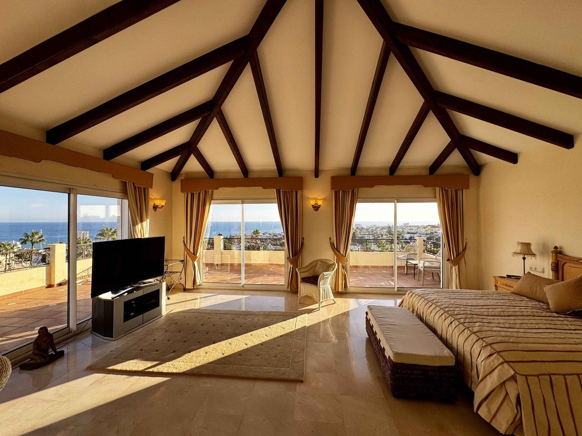 Spacious bedroom with large windows offering sea views, a private terrace, and exposed wooden ceiling beams.