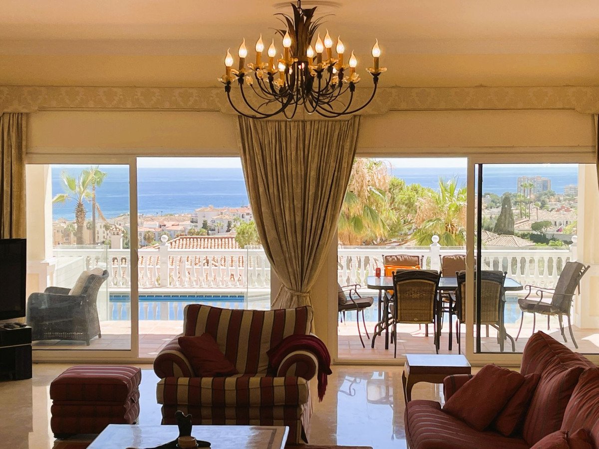 Living room with striped furniture, large windows overlooking the sea, balcony, and a pool.