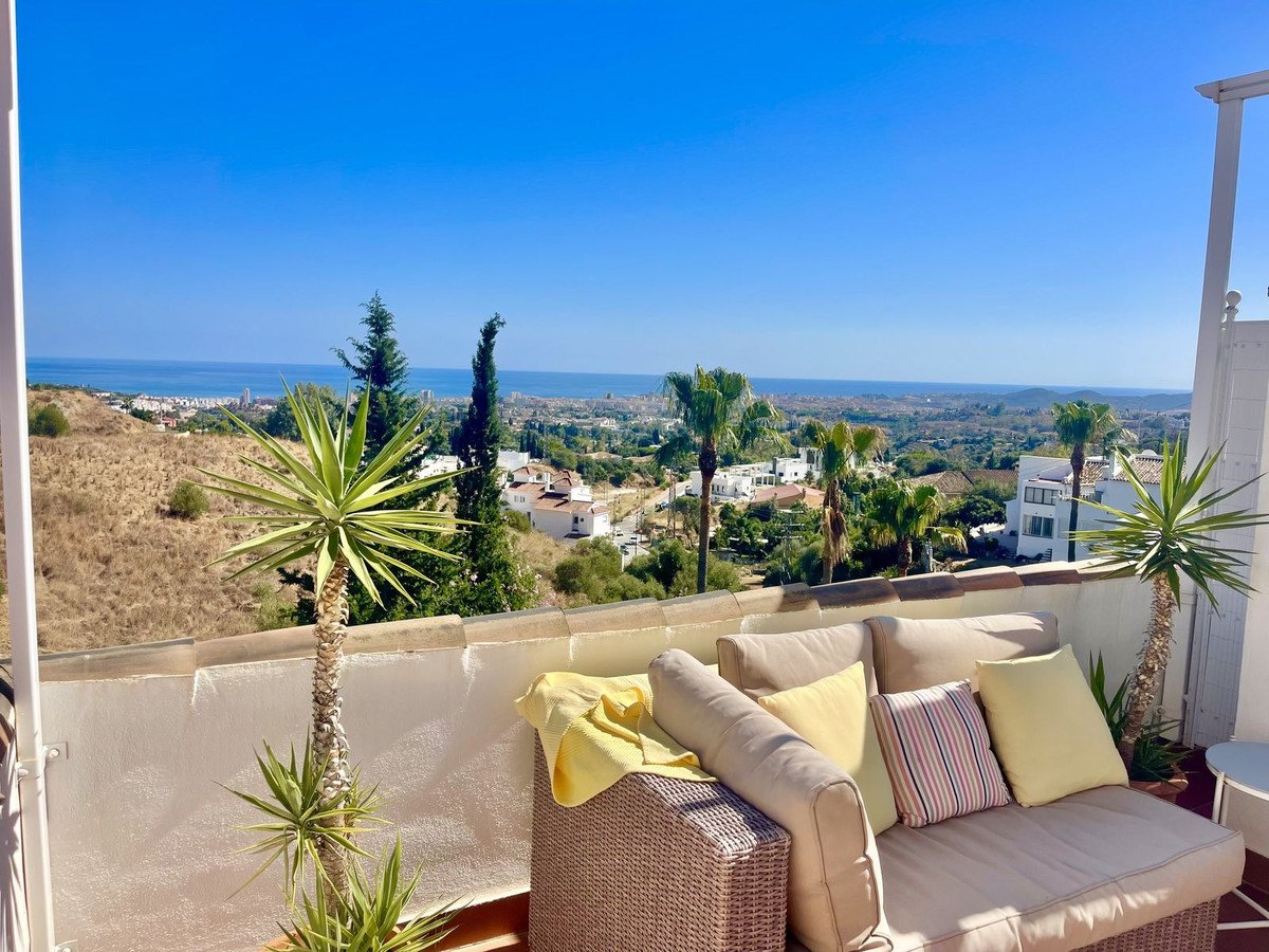 Terrace with comfortable sofa and cushions, overlooking a scenic view of palm trees and the sea.