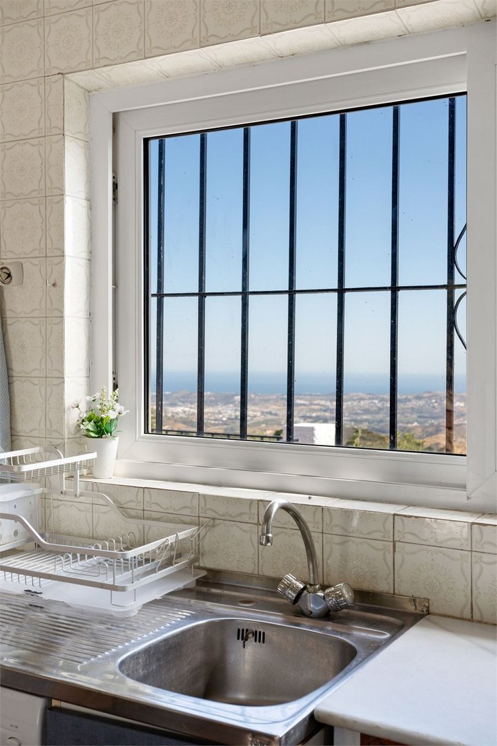 Kitchen sink with a metal faucet, drying rack, and a beautiful sea view through the window with bars.