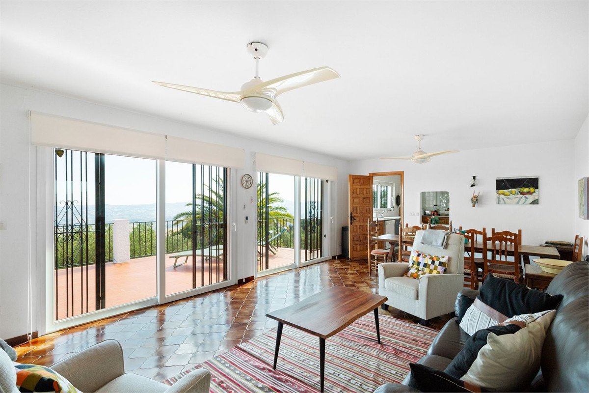 Spacious living room with large sliding doors opening to a terrace offering a sea view and lush greenery.