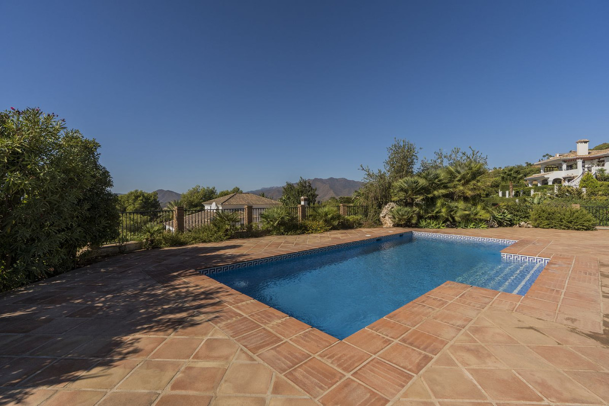 Outdoor swimming pool with clear blue water, surrounded by a tiled patio and lush greenery, with a mountain view.