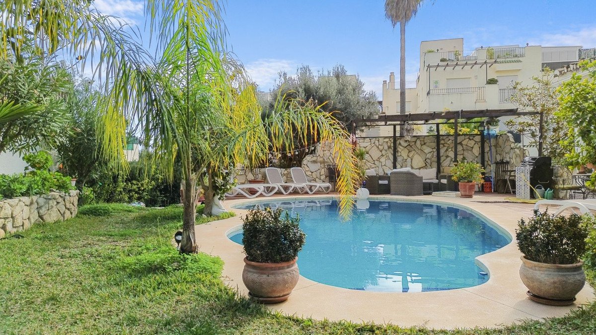 A curved swimming pool with lounge chairs and outdoor seating area surrounded by lush greenery and palm trees.