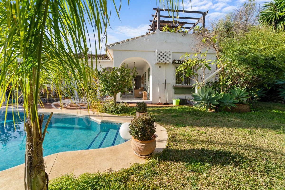 A white villa with a blue swimming pool, patio, and lush green garden under a clear blue sky.