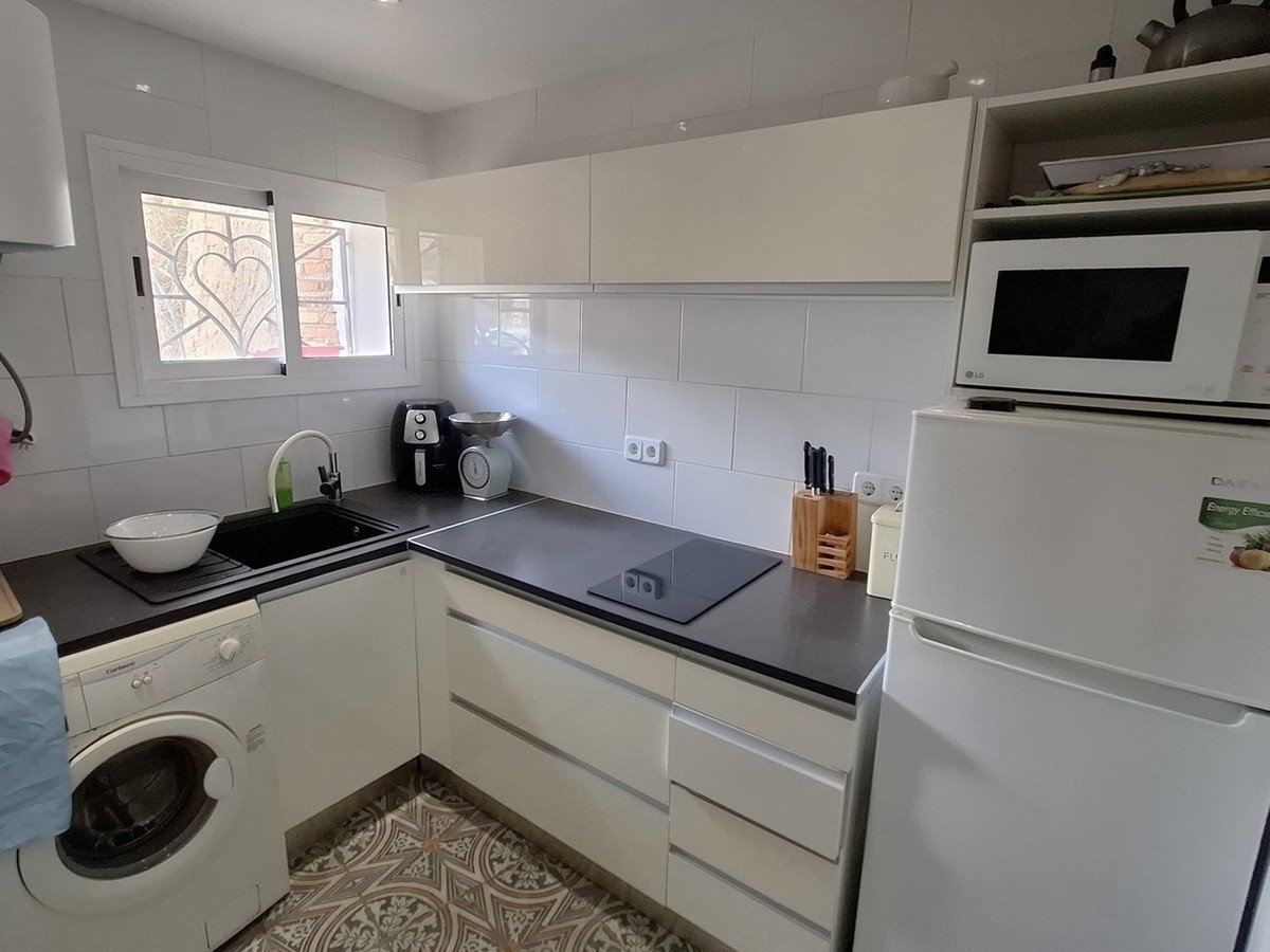 Modern white kitchen with dark countertops, sink, washing machine, refrigerator, microwave, and tiled floor.