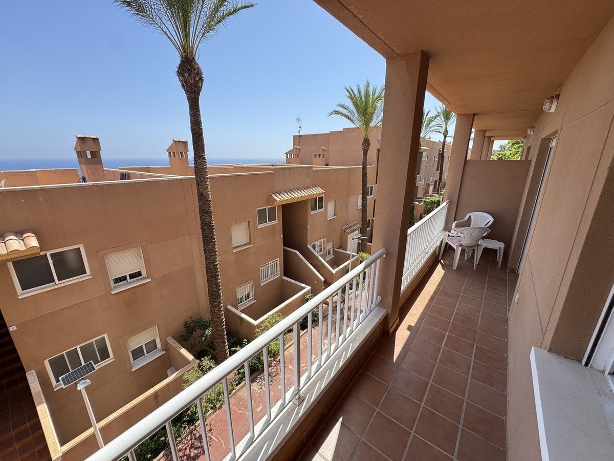 A spacious tiled balcony with white railing, offering a view of the sea and palm trees.