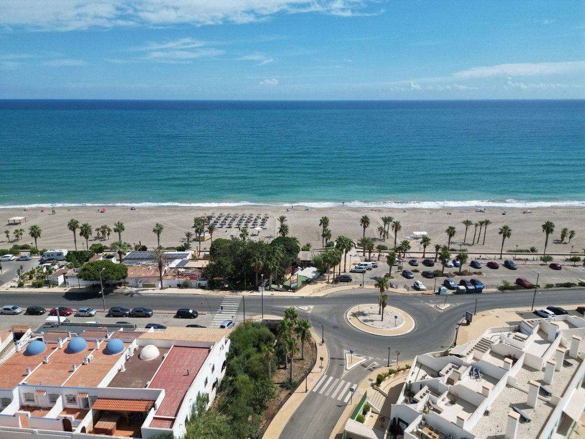 Aerial view of a resort with a beach, sea, palm trees, and parking lot in a coastal town.