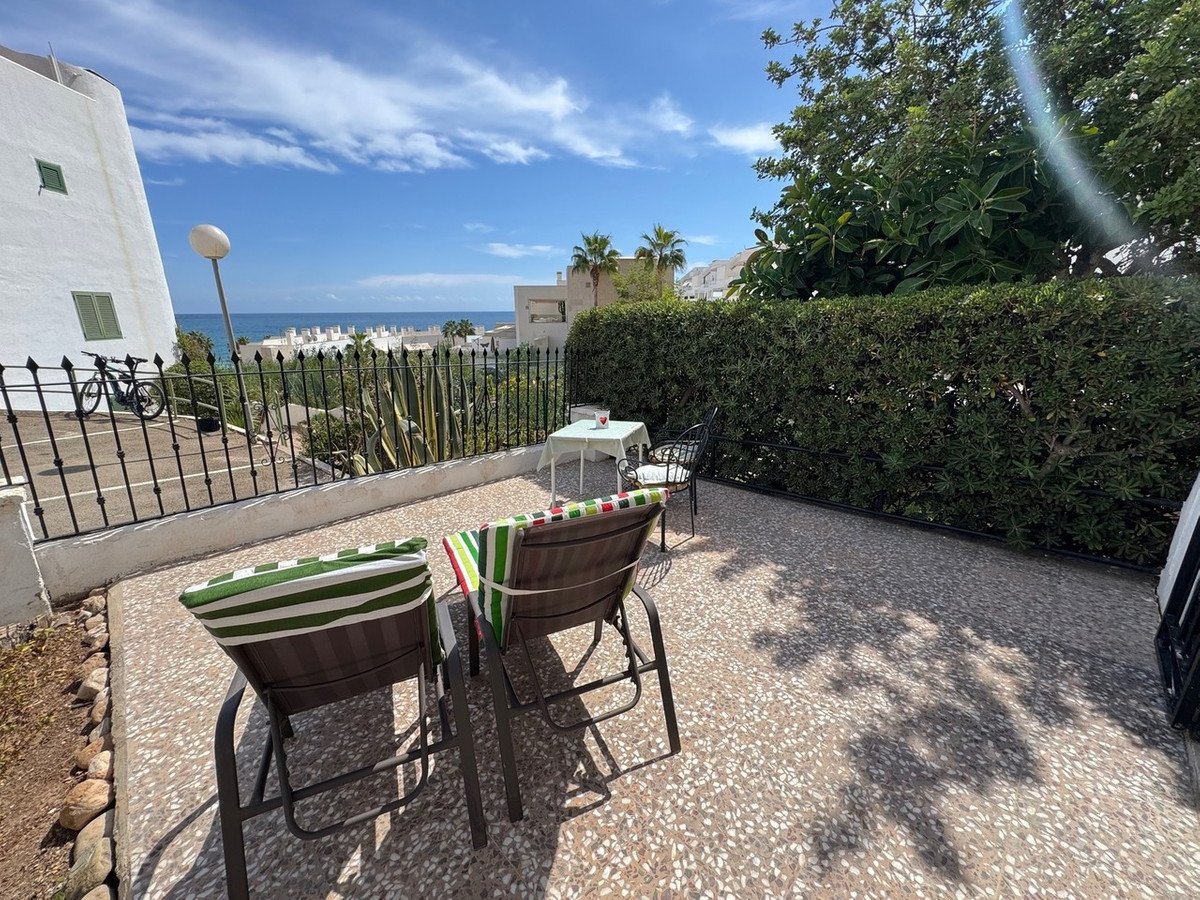 Terrace with outdoor seating and table offering a view of the sea and buildings in the distance.