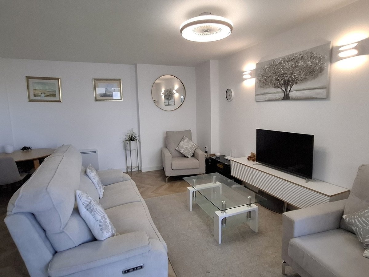 A modern living room with a sectional sofa, glass coffee table, TV unit, and decorative wall art.
