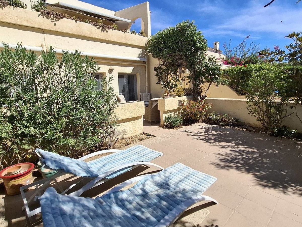 Sun loungers on a tiled terrace with lush green plants and a blue sky overhead.