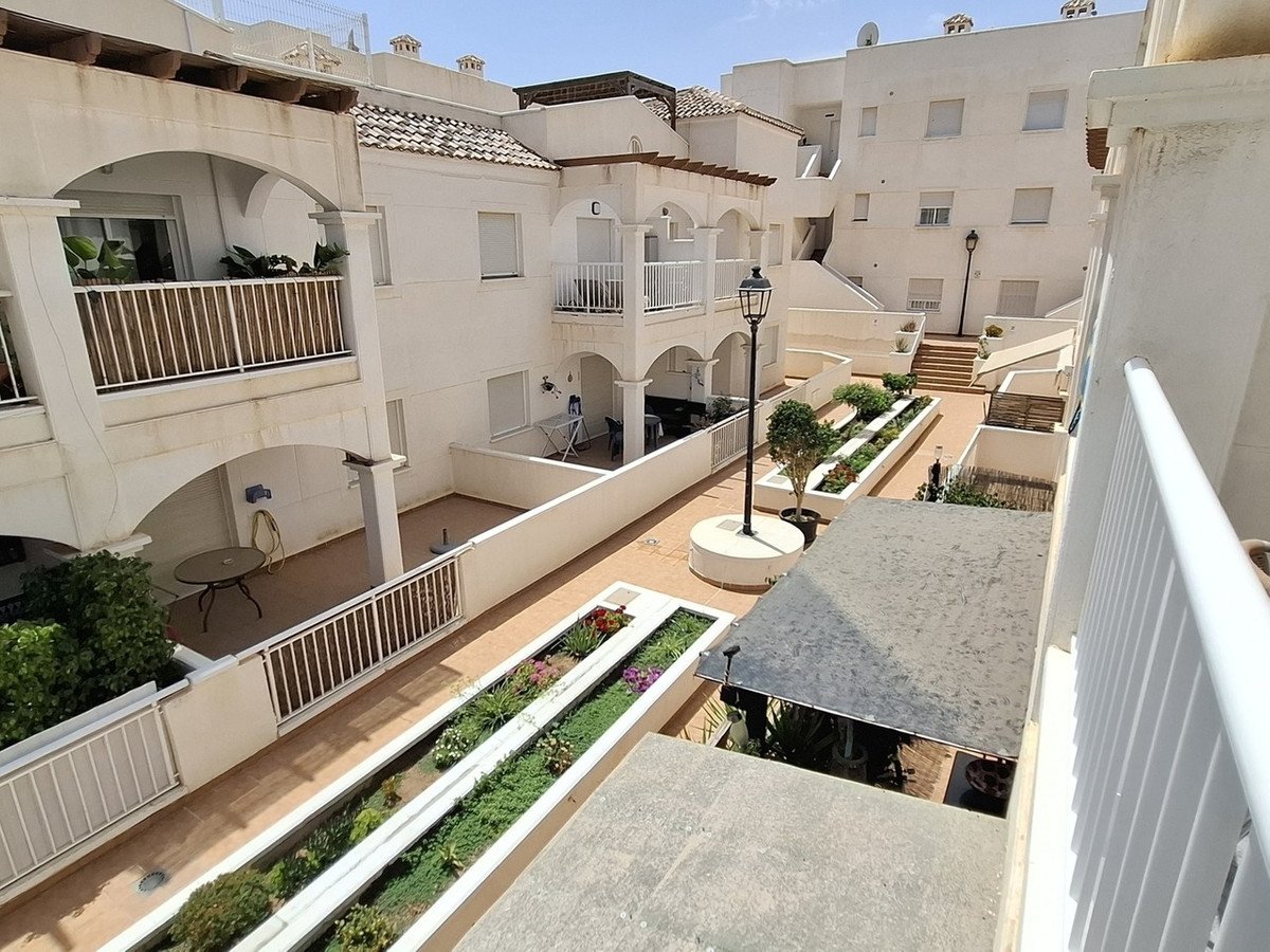 Apartment balcony view of white courtyard with arches, planters, and tiled walkways.