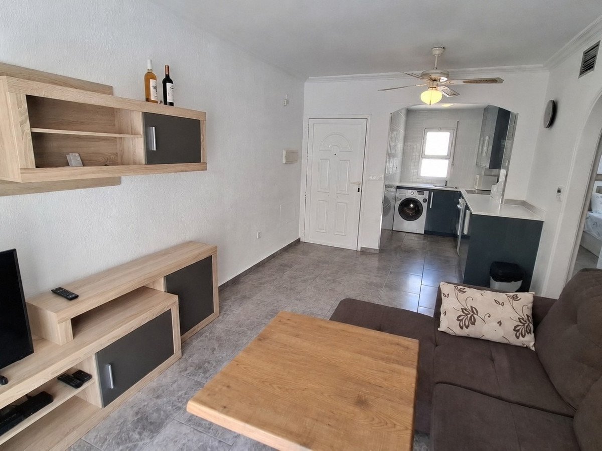 Modern living room with a kitchenette, featuring a sofa, TV unit, and a ceiling fan above the kitchen area.