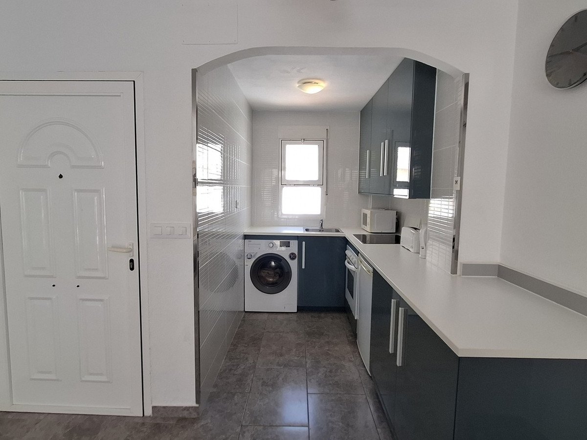 A modern kitchen with dark blue cabinets, white countertops, a washing machine, and a window.