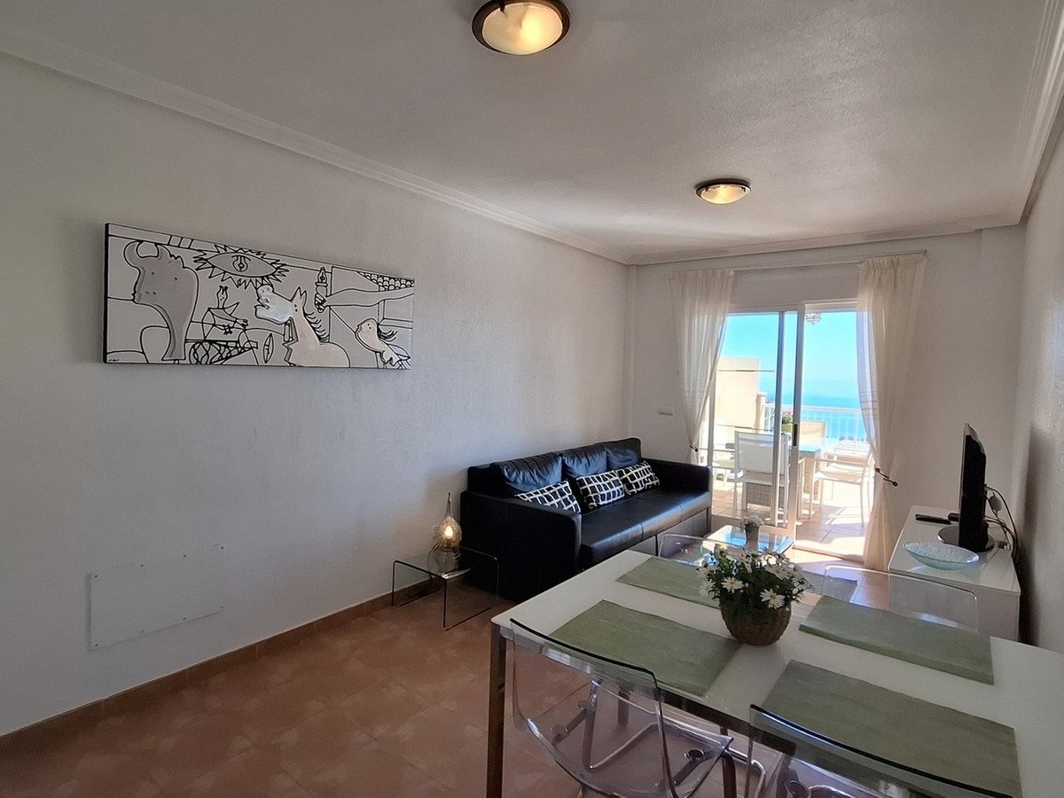 Living room with black sofa, dining table, and large sliding doors opening to a balcony with a sea view.