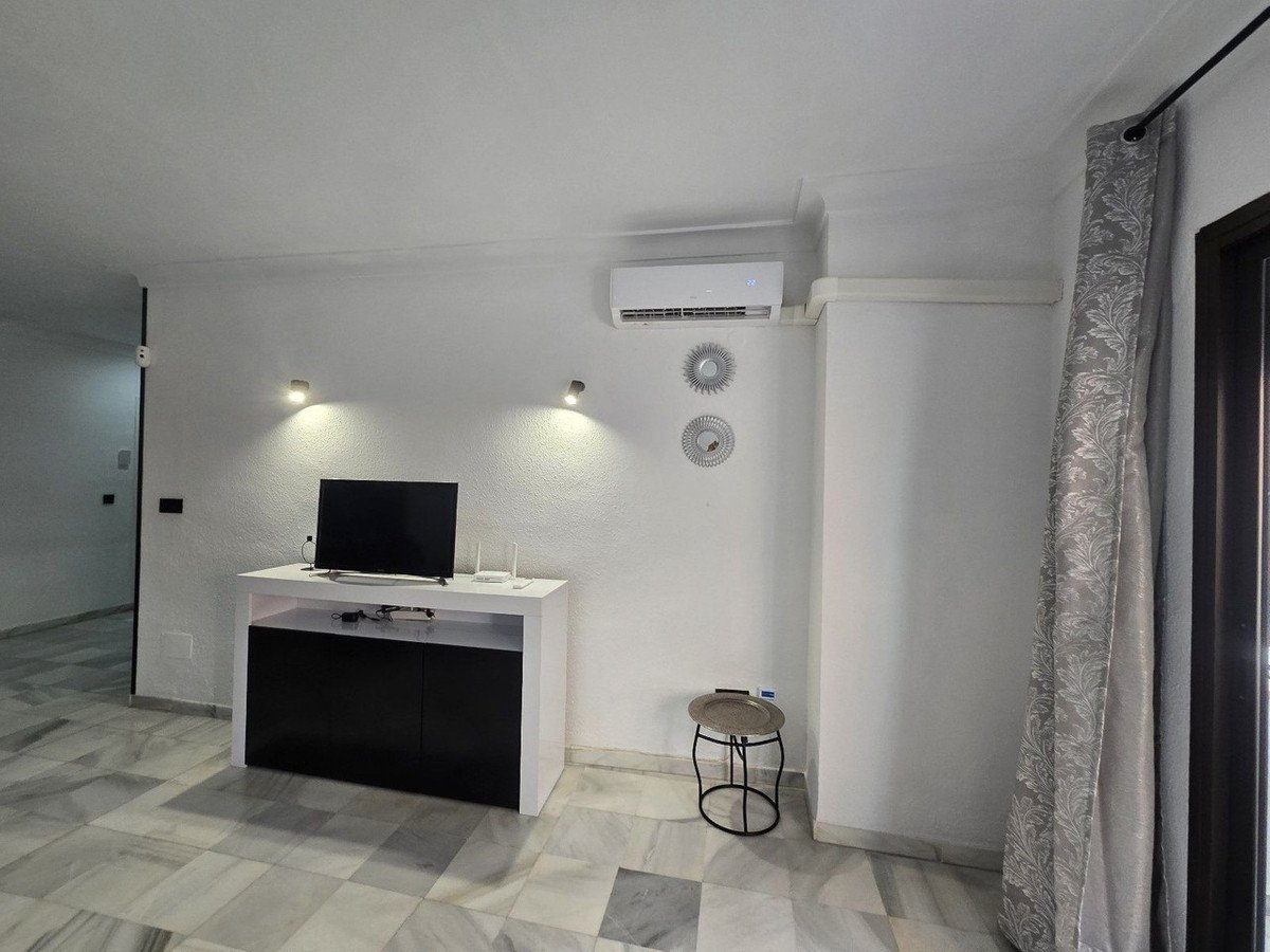 A bright living room with a TV stand, air conditioner, and marble flooring.