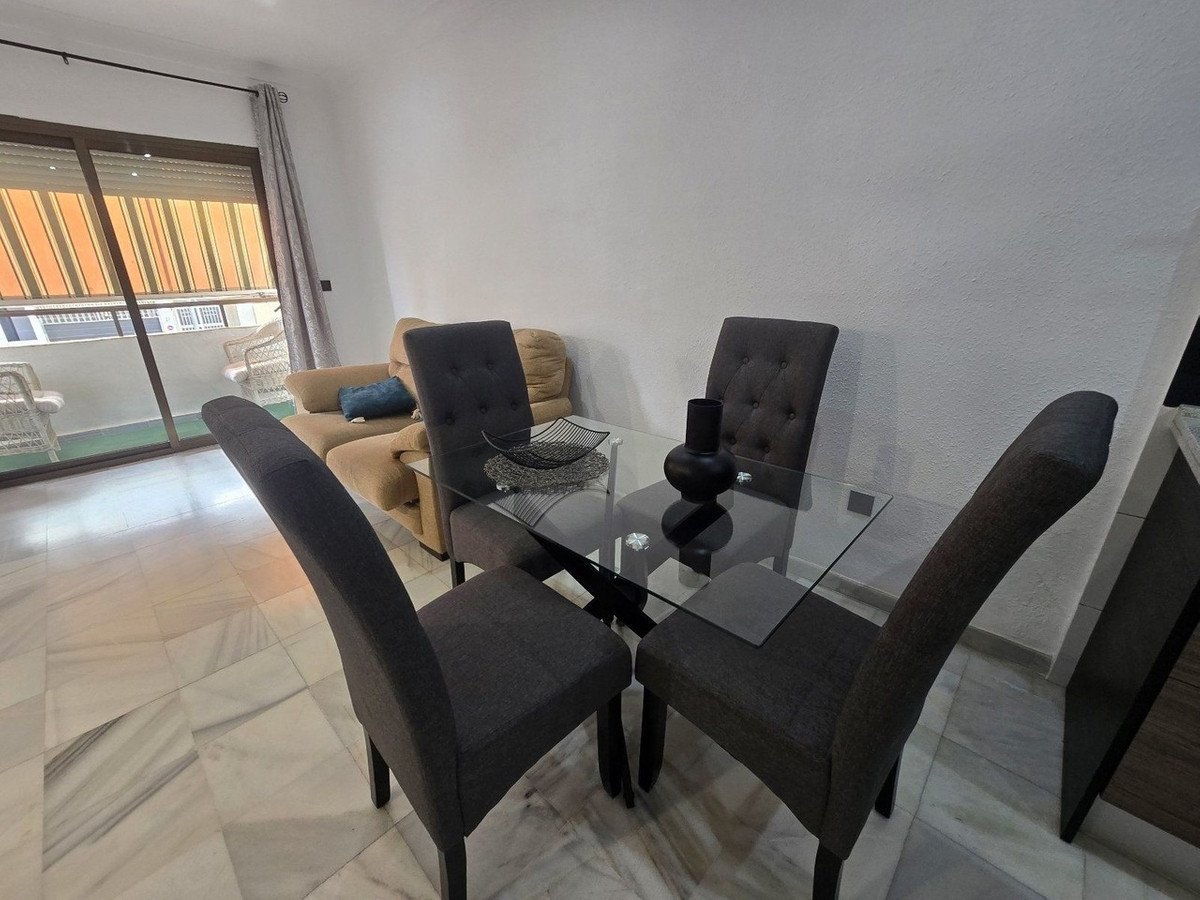 A dining area with a glass table, four chairs, and a view of a balcony with striped curtains.