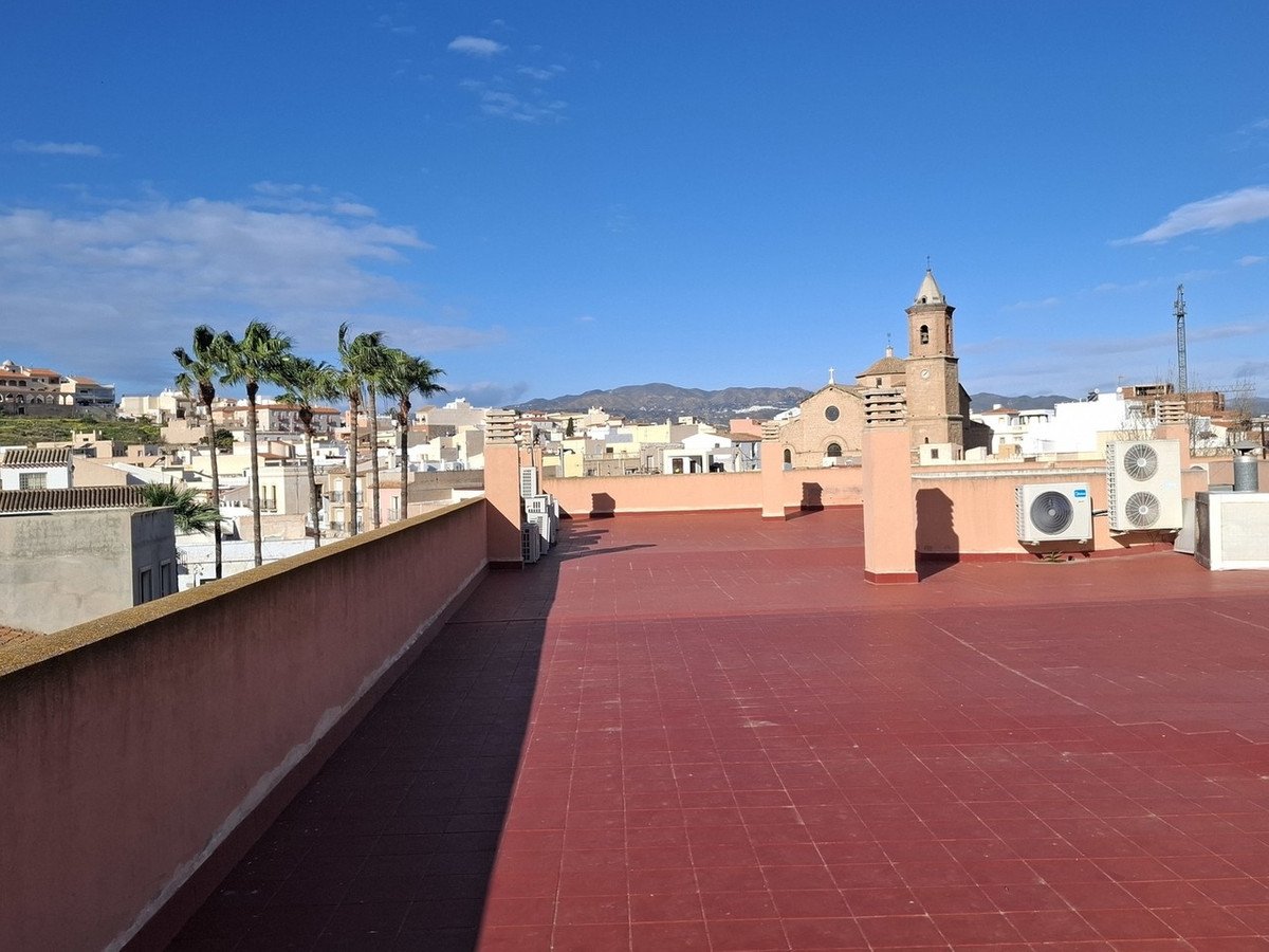 Rooftop terrace with red tiles, overlooking a town with palm trees and a church spire under a blue sky.