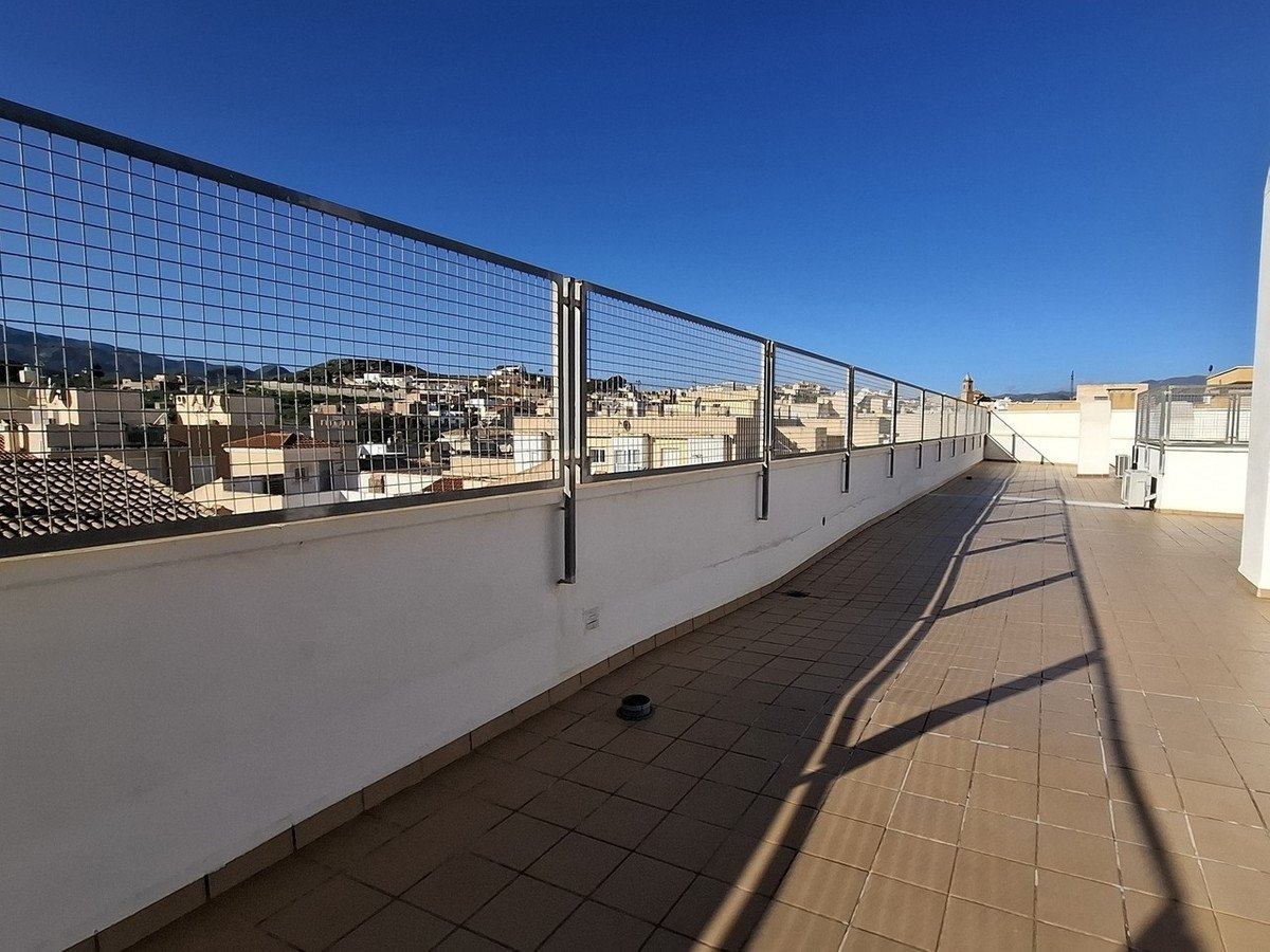Spacious tiled terrace with a metal railing overlooking a sunny urban landscape with buildings and hills under a clear blue sky.