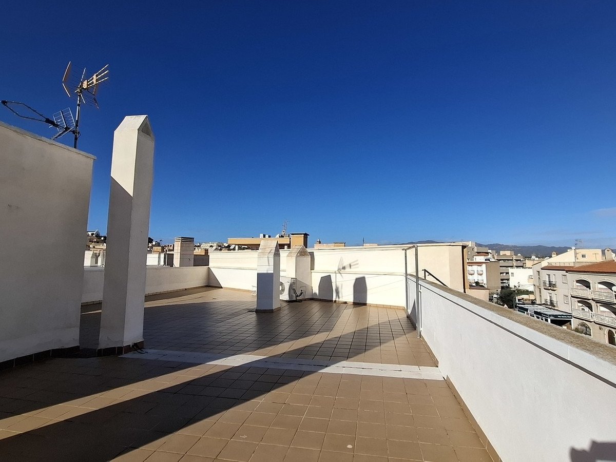 Spacious tiled terrace with white railings, offering a panoramic view of surrounding buildings under a clear blue sky.