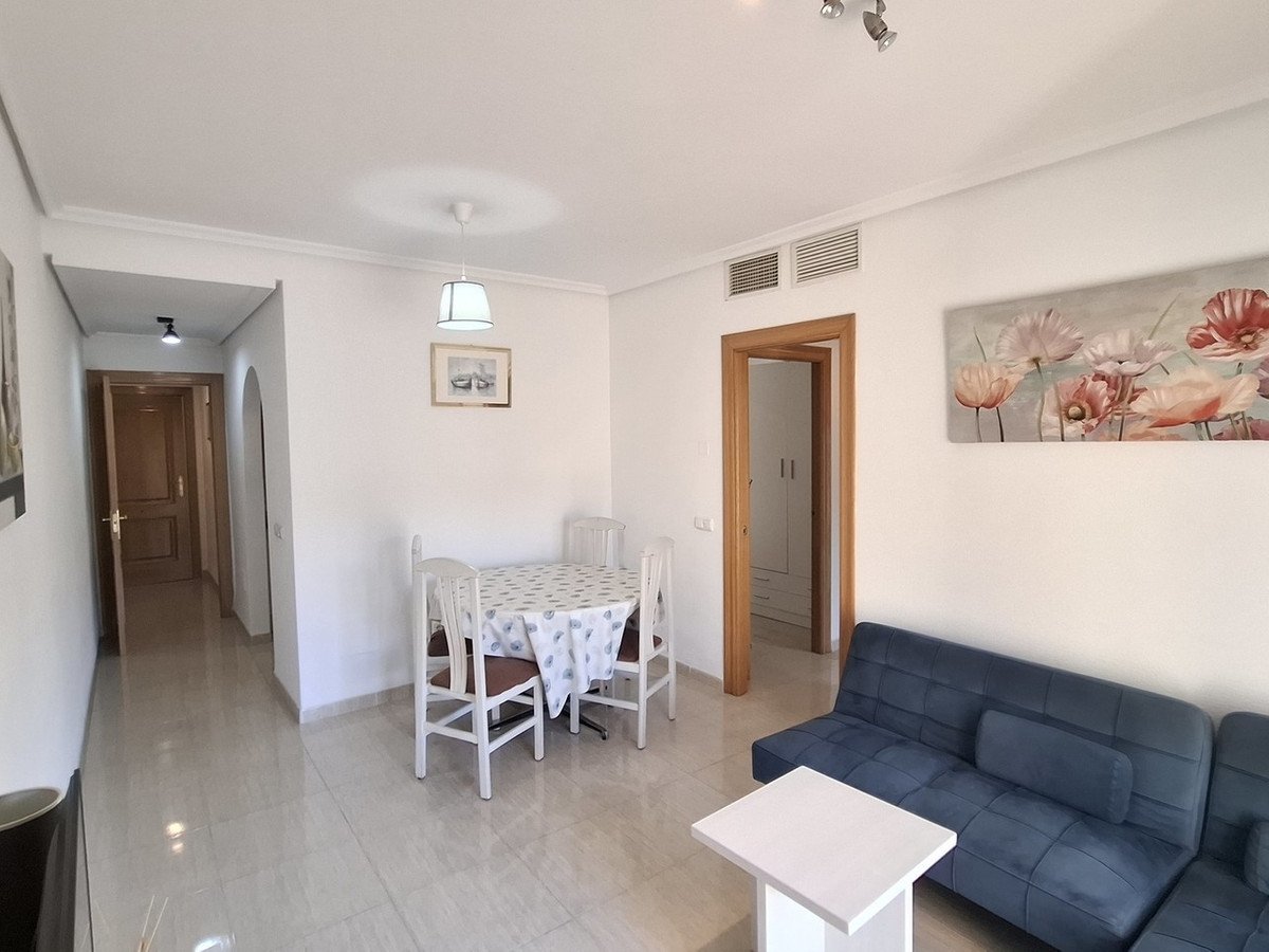 A modern living and dining area with a blue sofa, dining table, chairs, and artwork on the wall.