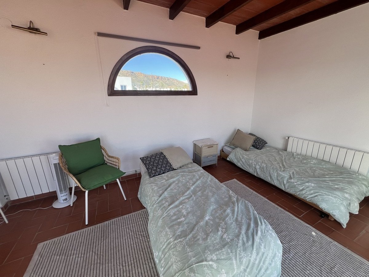 Bedroom with two single beds, green chair, and mountain view through arched window