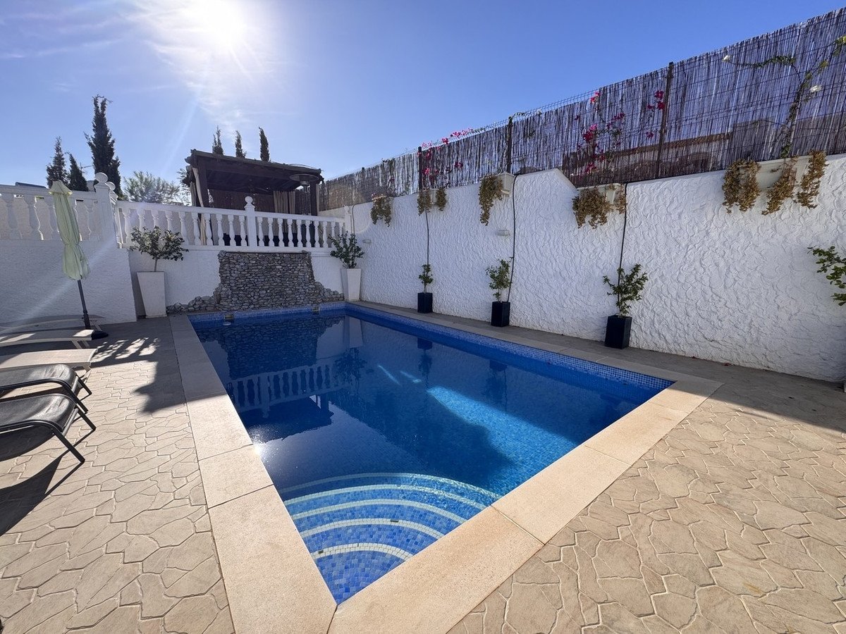 Private swimming pool with sun loungers, white walls, and potted plants.