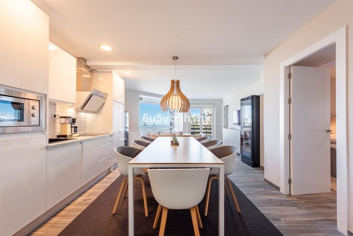Modern kitchen and dining area with a large table, chairs, and a panoramic window offering a sea view.