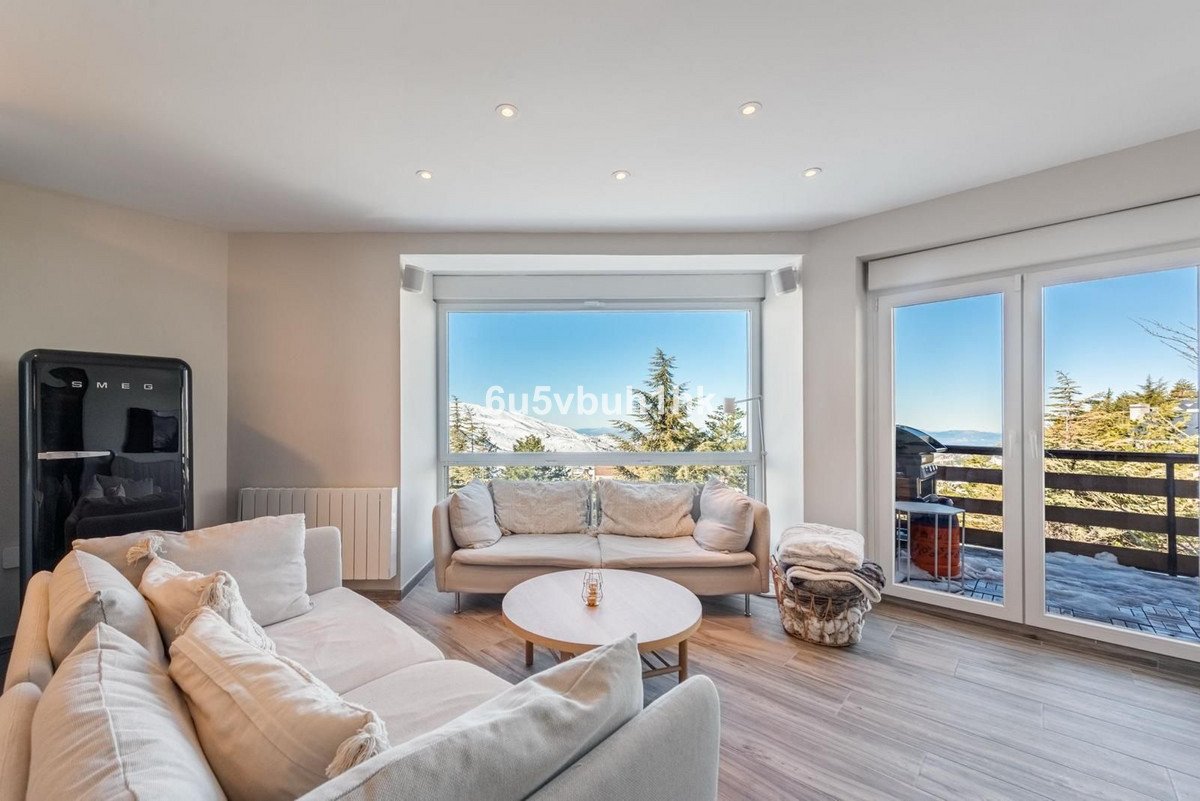 Living room with comfortable sofas, a large window showcasing a stunning mountain and forest view, and a balcony access.