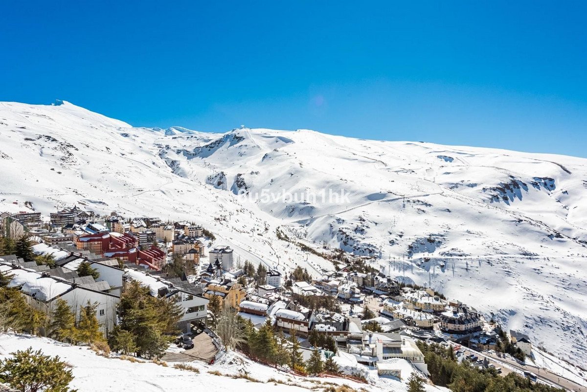 A picturesque ski resort village nestled in a snow-covered mountain range under a clear blue sky.