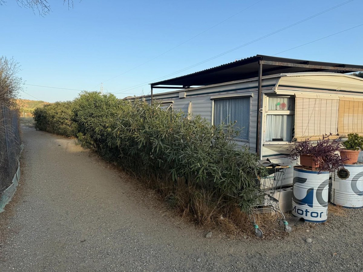 Exterior of a mobile home with green foliage and a gravel pathway leading to it.