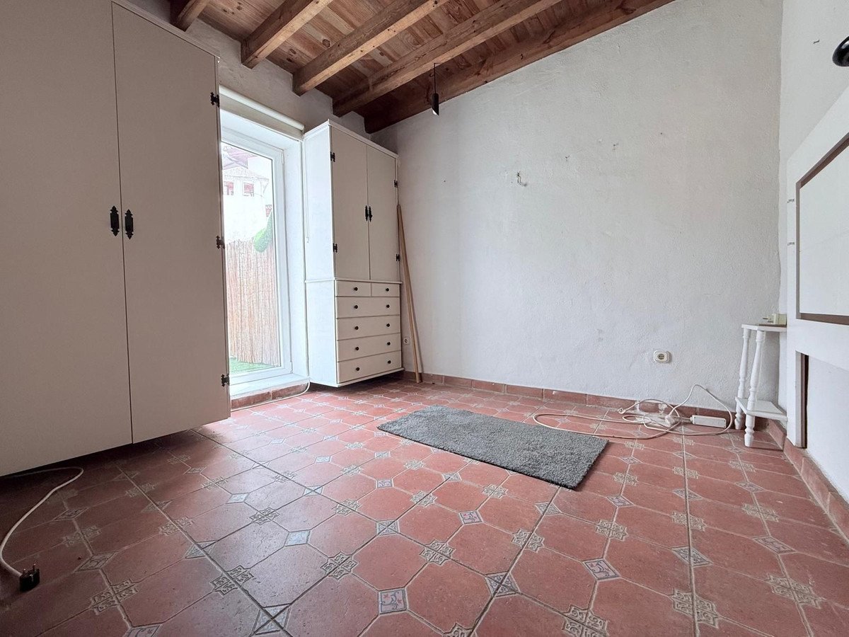 A room with two large wardrobes, a dresser, tiled floor, exposed wooden ceiling beams, and a window leading to a garden.