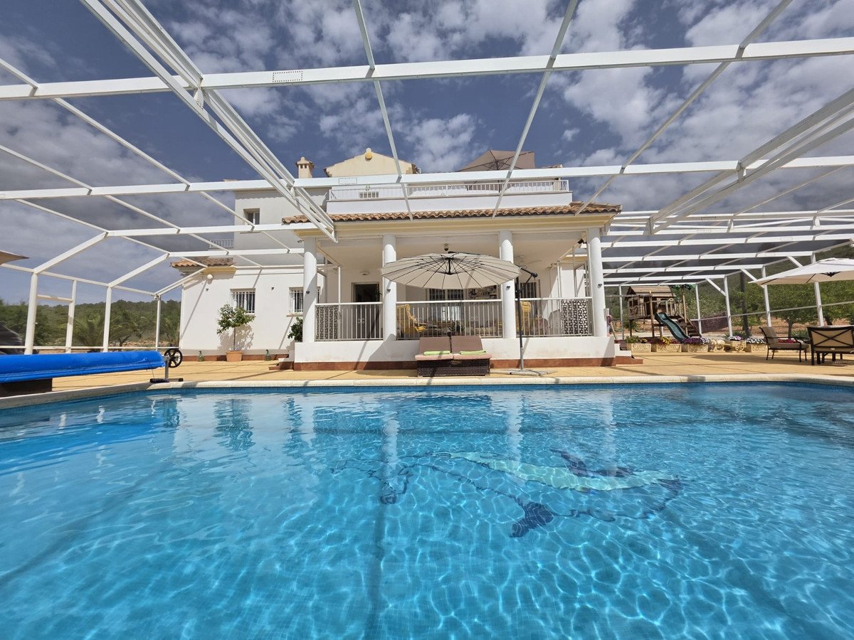 Beautiful villa with a large swimming pool, covered patio, lounge chairs, and a children's play area visible in the background.