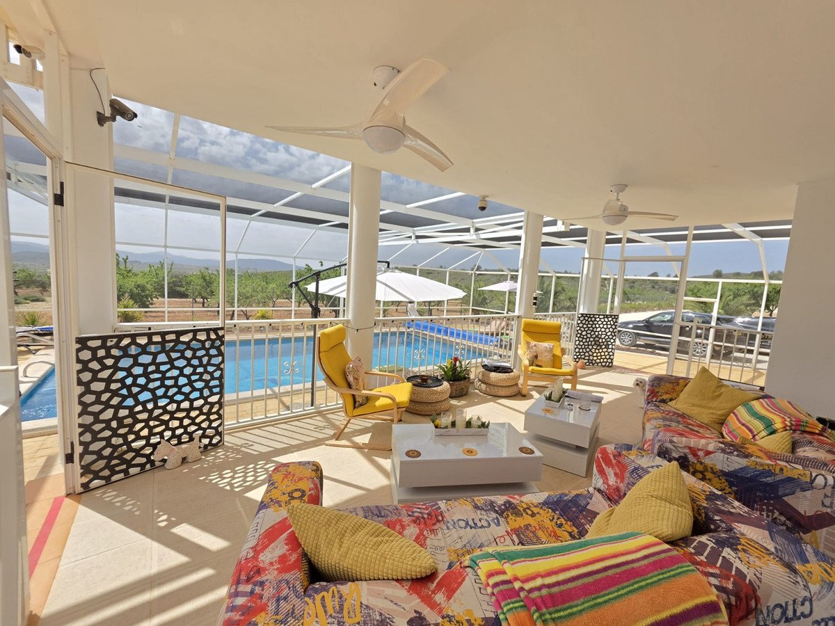 Sunroom with comfortable seating, ceiling fans, and views of a swimming pool and surrounding landscape.
