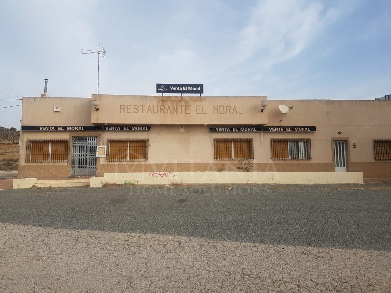 A single-story restaurant with a beige exterior, featuring multiple windows and a satellite dish.