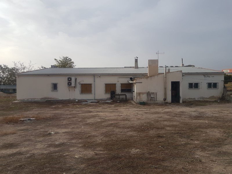 Exterior view of a single-story building with an air conditioning unit and barred windows under a cloudy sky.