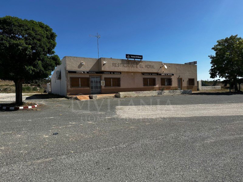 Single-story restaurant with outdoor seating, clear blue sky, gravel parking area.