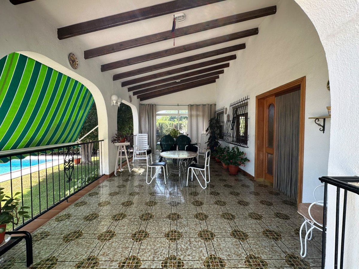 Covered patio with pool view, seating area, and striped awning. Features tiled floor and wooden beams on the ceiling.