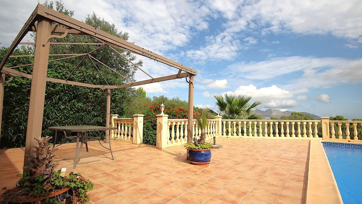 Terrace with a pergola, table, railing, potted plants, and a swimming pool with a mountain view.