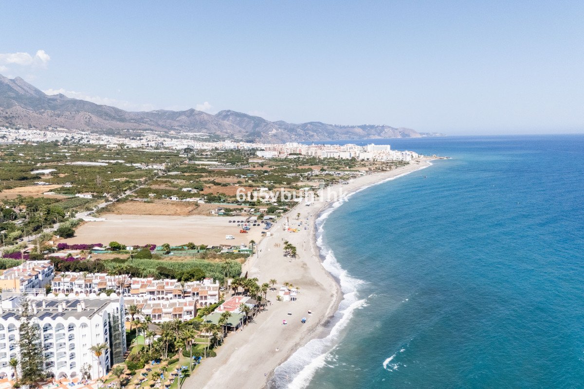 Aerial view of a beachfront resort town with a sandy beach, turquoise sea, and mountains in the background.