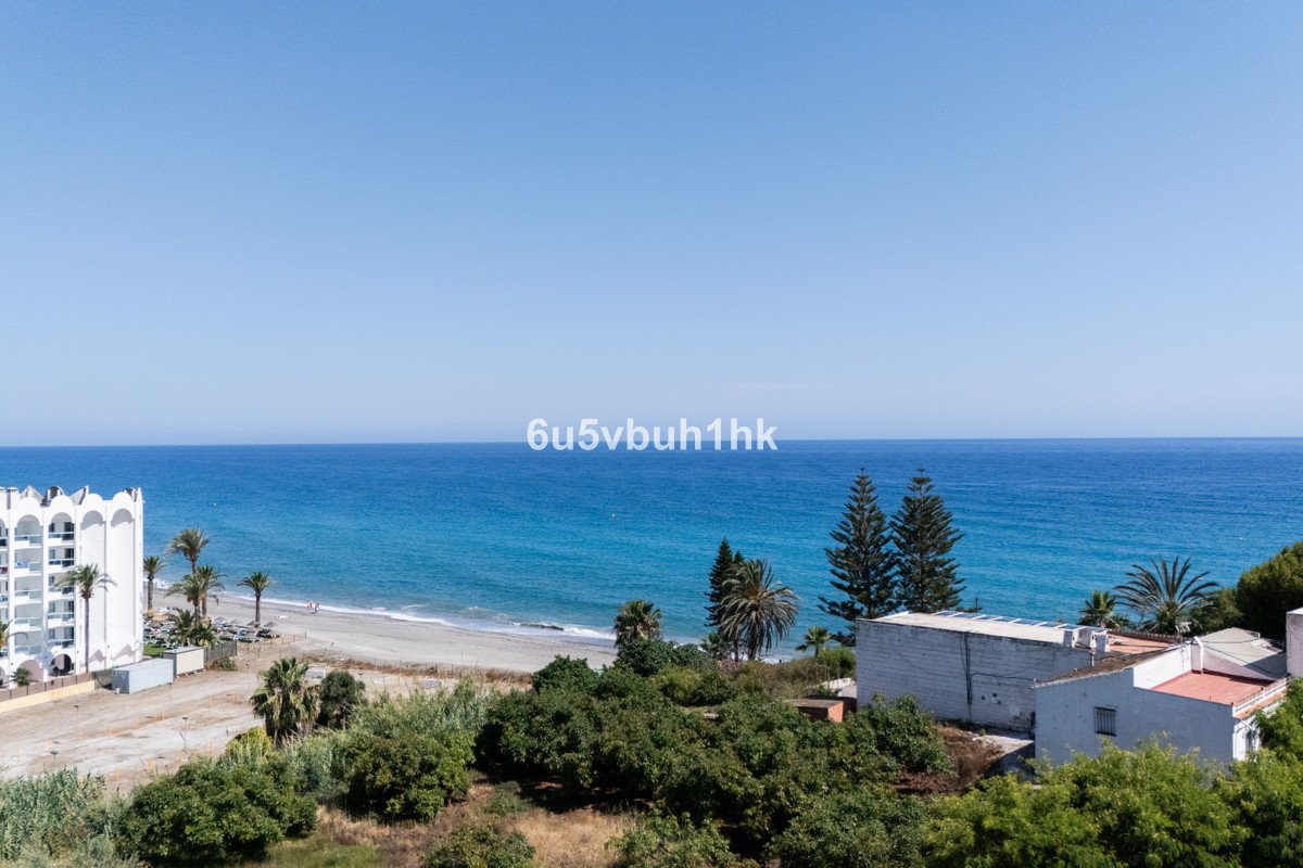 View from a balcony overlooking a beach, blue ocean, and lush greenery under a clear sky.